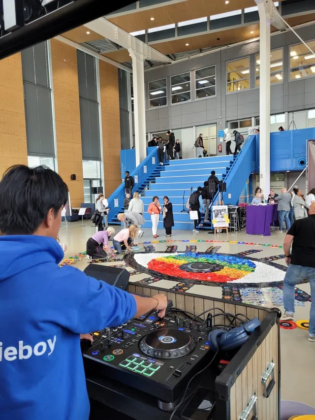 Tjinnakon draait in een schoolhal terwijl bezoekers op de vloer een kunstwerk leggen.